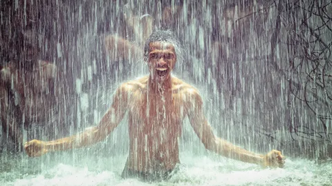 A photo of a young man wildly celebrating under a waterfall. Illustrates [alt text].