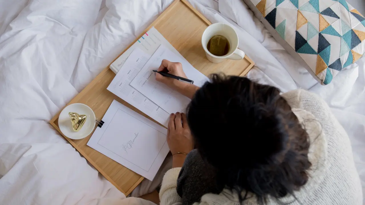 A photo showing a view from above of a woman taking organized notes with stickys and even a tea mug.