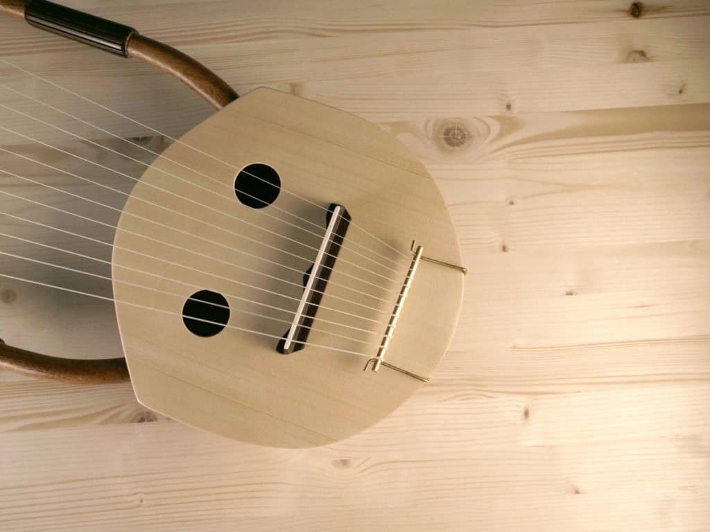 A pale wooden traditional lyre with dual sound holes and parallel strings laid on a knotted pine wood surface, photographed from above - an instrument similar to those played by Lyre Music RPG and featured in TTRPG settings