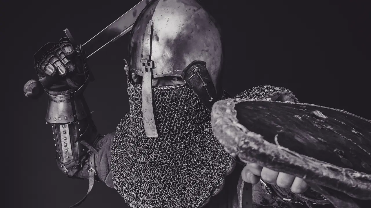 A black and white photo of a man wearing plate armor while charing for an attack with a sword and shield. Illustrates [alt text].