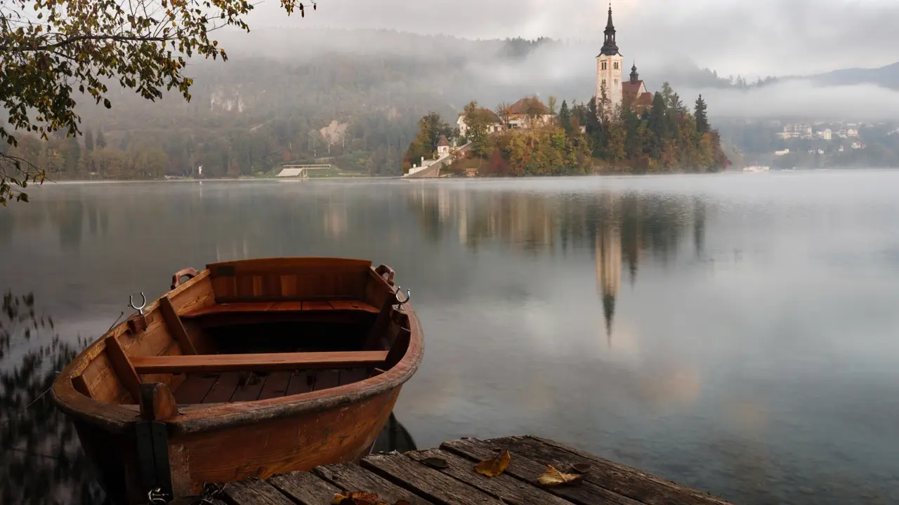 An early morning at Lake Bled with a brown wooden boat floating. Illustrates [alt text].