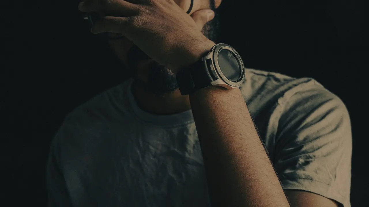 A photo of a man in a black background wearing a watch and facepalming in frustration. Illustrates [alt text].