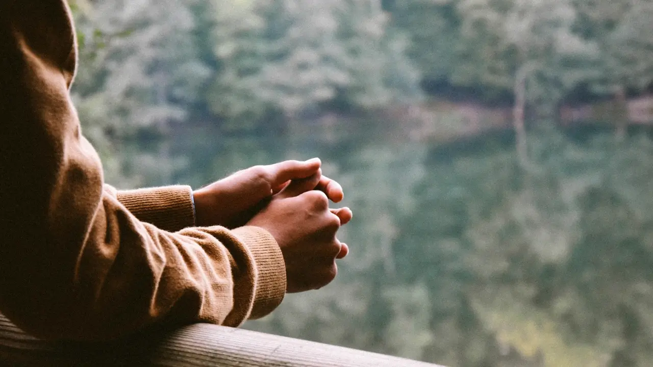 A tilt-shift photography of a person in a brown jacket thinking by a pond. Illustrates [alt text].