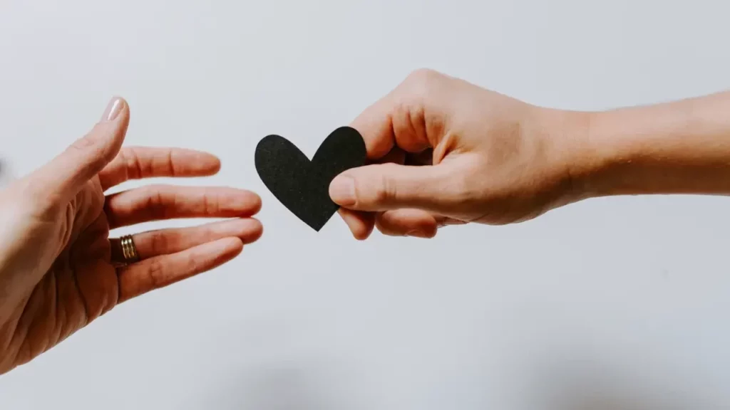 person-reaching-black-heart-cutout-paper Man handing a woman a heart shape.