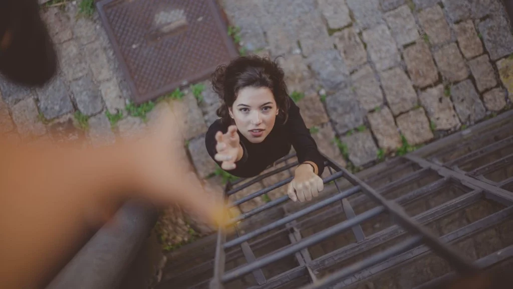 Photo of a woman on a ladder reaching up to a hand for help