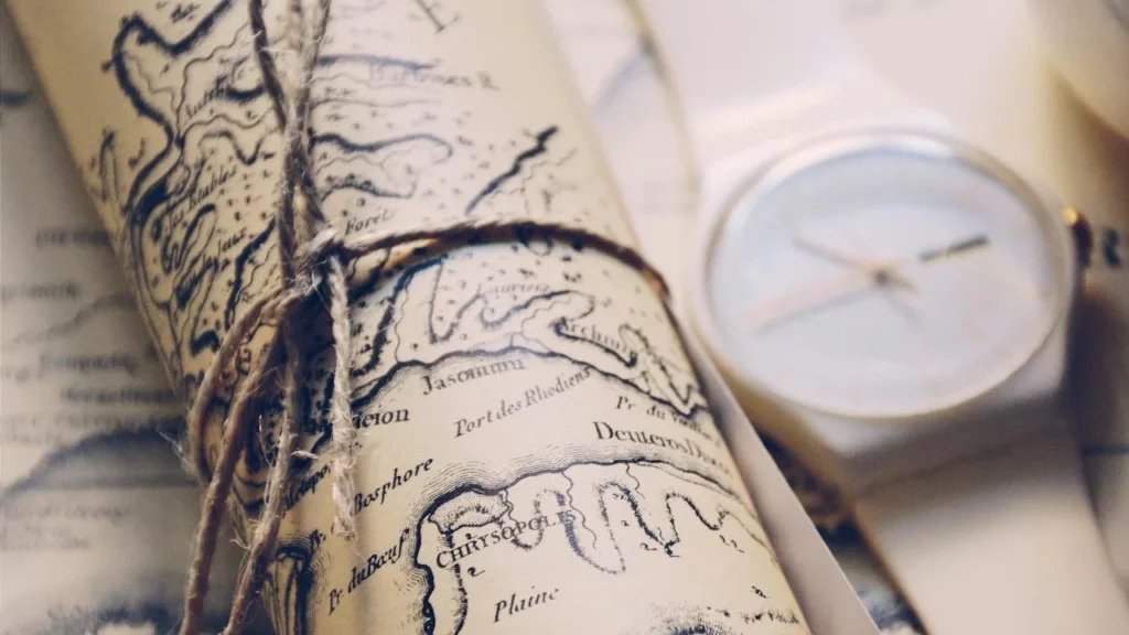 A photo of a parchment map of the Caribbean rolled up and tied with string next to a compass.