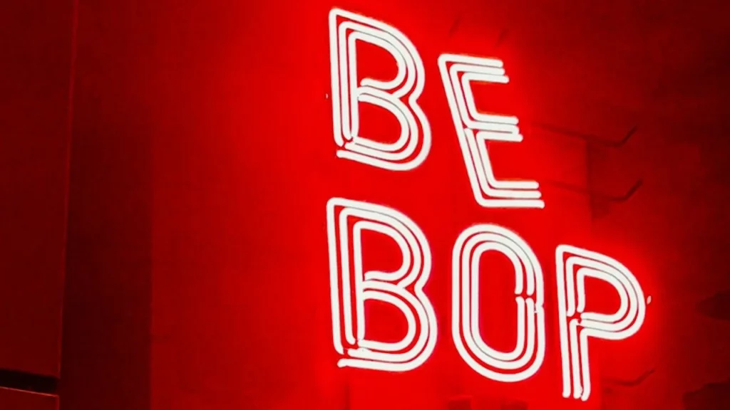 Photograph of a red neon sign reading "Be Bop" on a cafe wall.