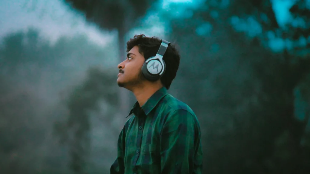 Man in green and black plaid dress shirt wearing black and white headphones. Themes of personal use.