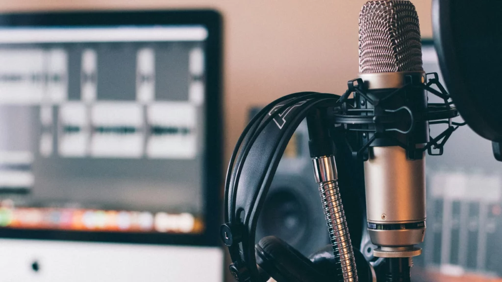 Home studio podcasting setup with microphone, headphones, desk stand with pop shield and computer. Themes of podcasts.