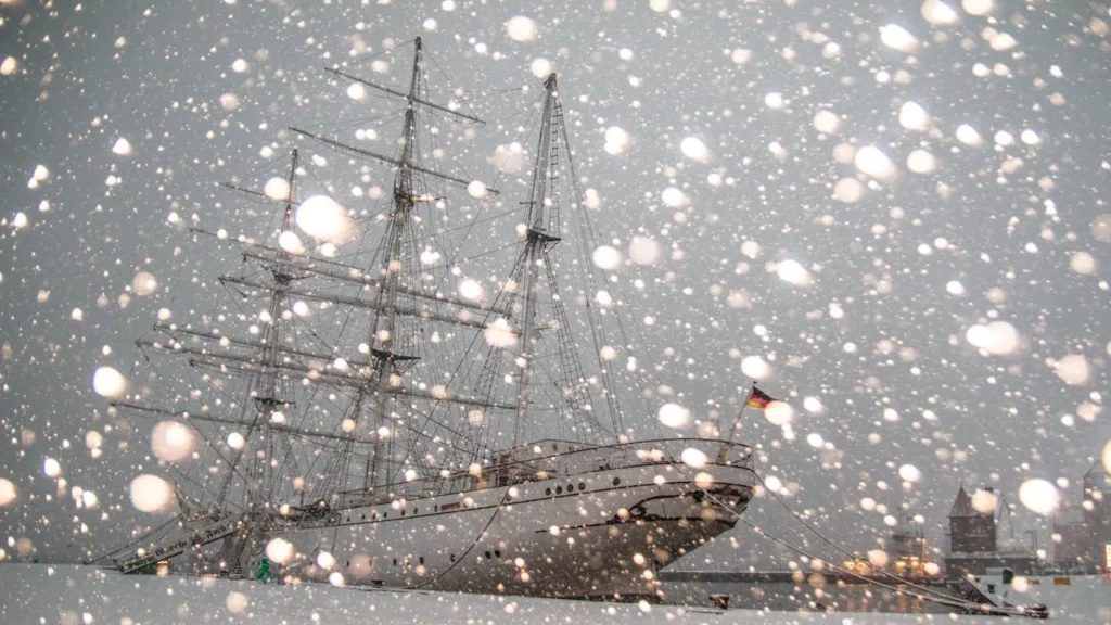 A photo of an old sail ship in blizzard conditions anchored in port.