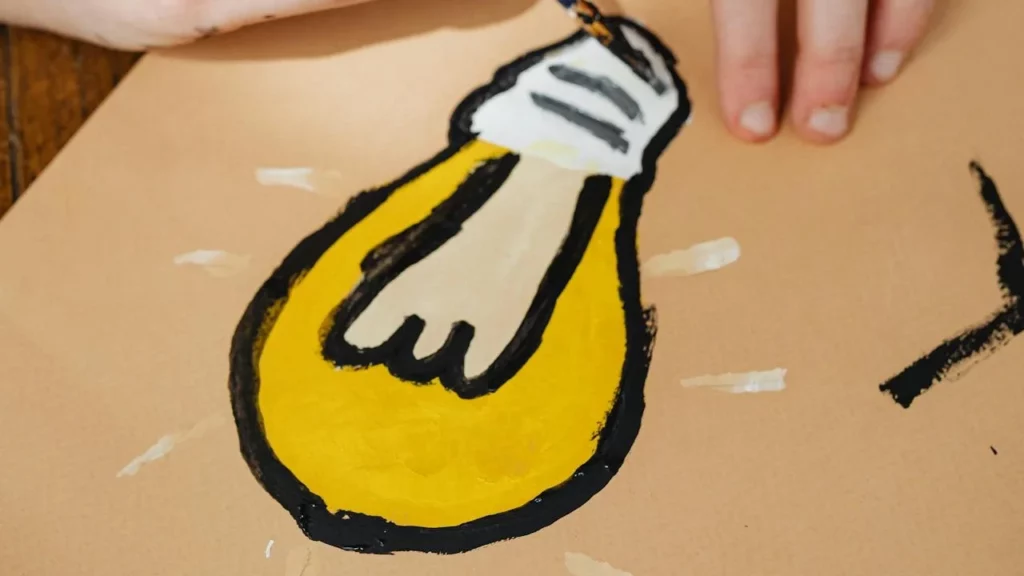 A photo of someone drawing a lightbulb on cardboard