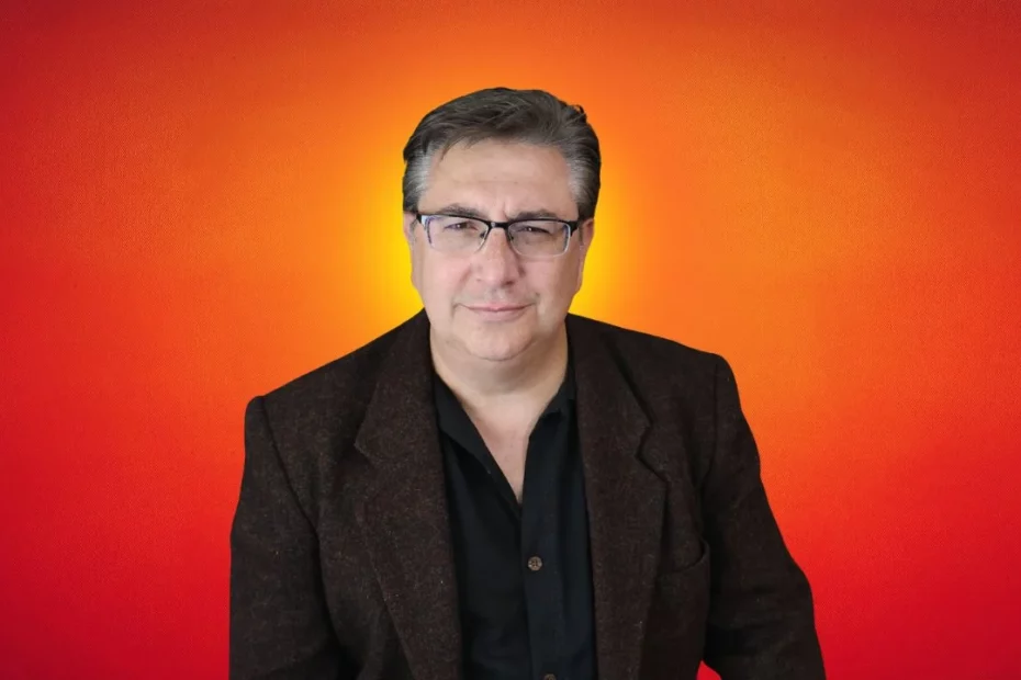 A headshot photo of Professor DM with an orange-red background.