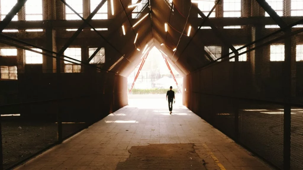 Photo of a person walking towards a bright light in an industrial building.