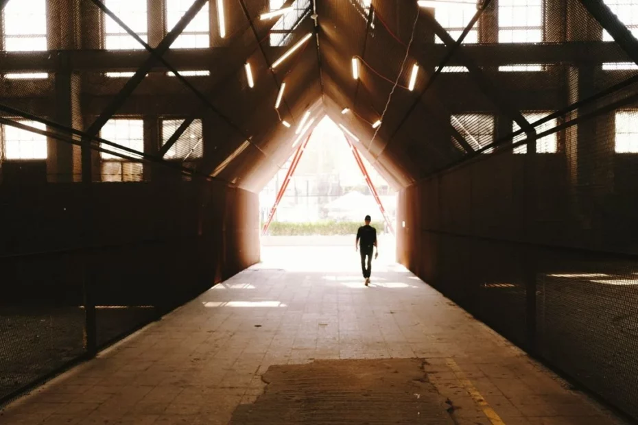 Photo of a person walking towards a bright light in an industrial building.